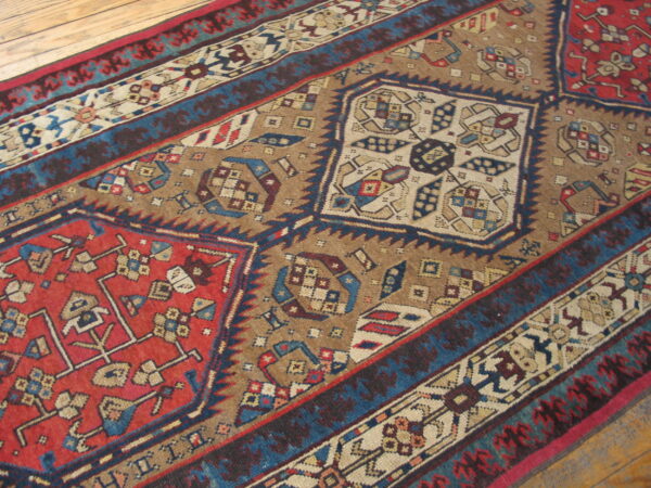 Geometric rug pattern featuring large red, blue, and tan stepped diamonds on a light wood floor.