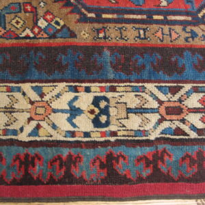 Knotted rug detail featuring alternating geometric borders in deep blue, red, tan, and cream.