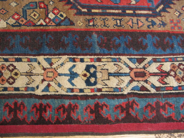 Knotted rug detail featuring alternating geometric borders in deep blue, red, tan, and cream.