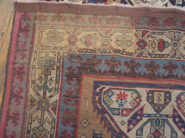 Geometric patterned rug corner in tan, blue, dark brown, and red resting on worn wood planks.