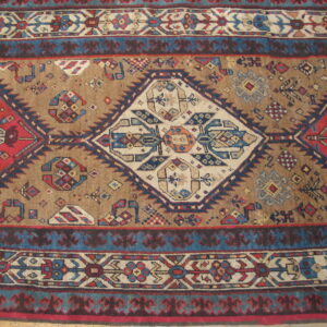 Detailed view of a geometric rug with a tan field, central cream medallion, red patterns, and multiple blue borders.