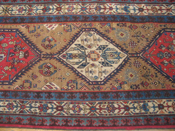 Detailed view of a geometric rug with a tan field, central cream medallion, red patterns, and multiple blue borders.