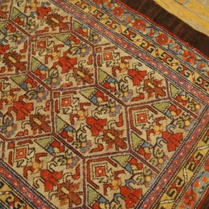 A rustic low-pile rug featuring a geometric pattern in red, blue, gold, and tan on wooden flooring.
