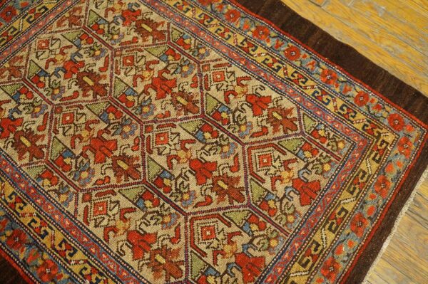 A rustic low-pile rug featuring a geometric pattern in red, blue, gold, and tan on wooden flooring.