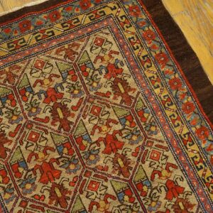 Angled view of a detailed multi-colored patterned rug with red, blue, and yellow borders on yellow wood flooring.