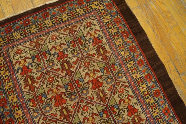 Angled view of a detailed multi-colored patterned rug with red, blue, and yellow borders on yellow wood flooring.