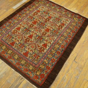 Small, low-pile rug with a geometric floral pattern in red, tan, blue, and green on light wood floor.