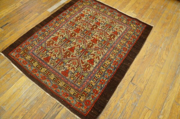Small, low-pile rug with a geometric floral pattern in red, tan, blue, and green on light wood floor.
