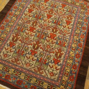The tan rug has red, blue, and gold geometric motifs and thick dark borders on hardwood flooring.
