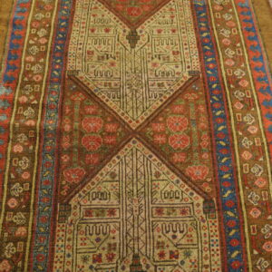 Intricate geometric rug in brown, beige, red, and blue tones displayed on light wood floorboards.