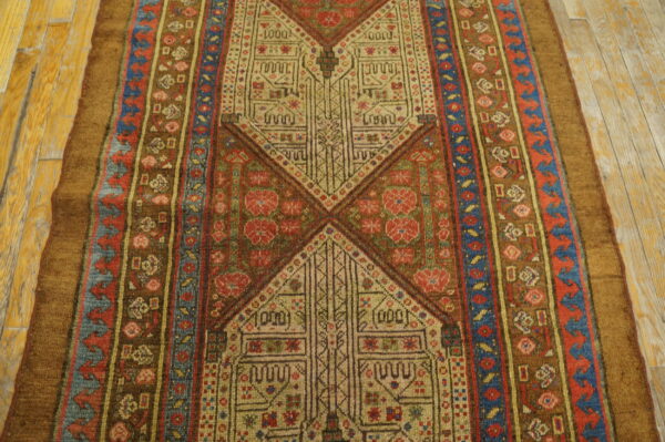 Intricate geometric rug in brown, beige, red, and blue tones displayed on light wood floorboards.