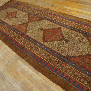 Long runner rug with complex geometric medallions in rust, beige, and blue on distressed wooden floorboards.