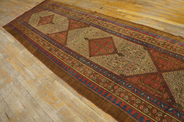 Long runner rug with complex geometric medallions in rust, beige, and blue on distressed wooden floorboards.