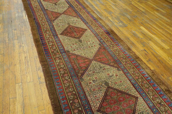 Muted earth tone runner with repeating geometric medallions sits on golden wood plank flooring.