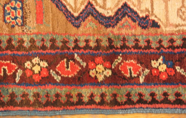 Detailed view of a high-pile rug with geometric and floral borders in rich reds, browns, and dark blues.