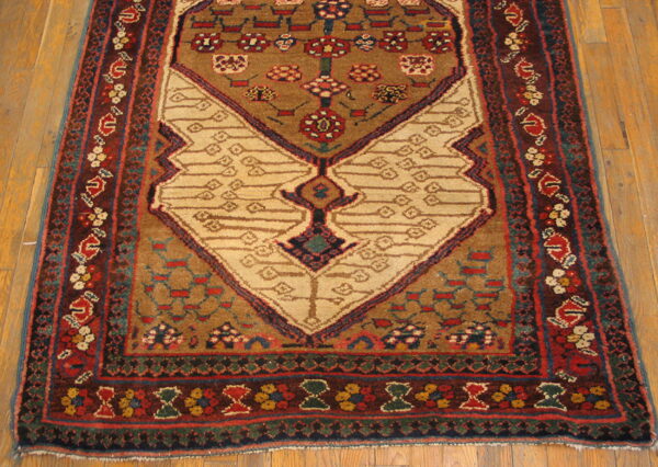 Brown and red rug with a prominent beige geometric motif rests on light wooden floorboards.