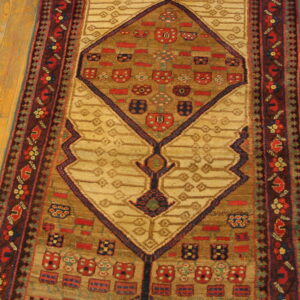 Geometric runner rug with tan and brown fields, complex red and navy motifs, lying on light wooden floorboards.