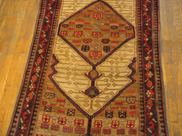 Geometric runner rug with tan and brown fields, complex red and navy motifs, lying on light wooden floorboards.