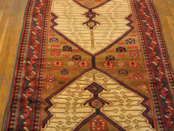 Geometric runner rug with alternating tan and brown fields, bordered by rust-red floral designs on wood.