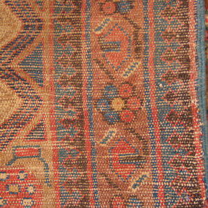 Flat-woven tan, red, and blue geometric rug lying adjacent to a brown textured pile rug.