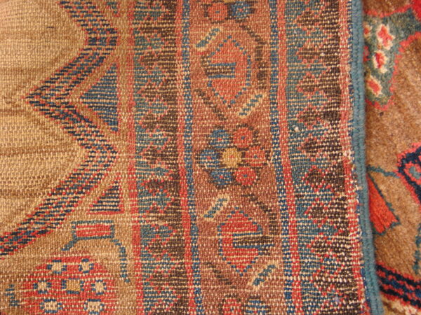 Flat-woven tan, red, and blue geometric rug lying adjacent to a brown textured pile rug.