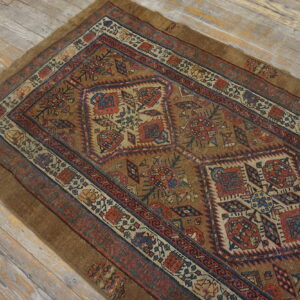 Brown geometric low-pile rug with red and blue accents displayed on light weathered wood flooring.