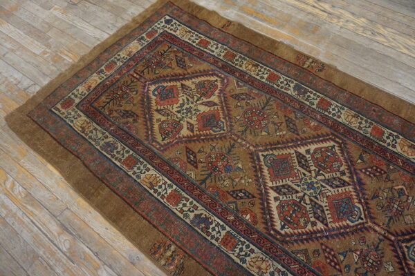 Brown geometric low-pile rug with red and blue accents displayed on light weathered wood flooring.