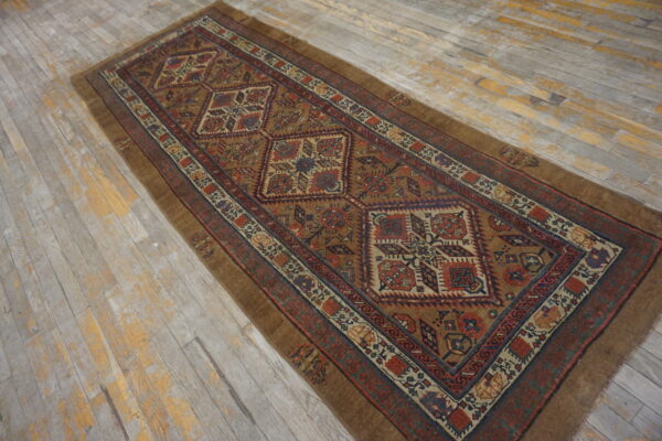 Brown runner rug with repeating geometric patterns in red and blue on weathered wood floors.