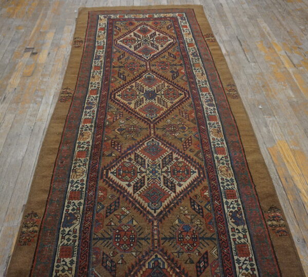 Geometric runner rug in browns, reds, and navy with large diamond motifs rests on worn wooden floorboards.
