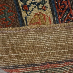 Close-up of a folded rug showing the woven brown backing and patterned red, blue, and tan pile.