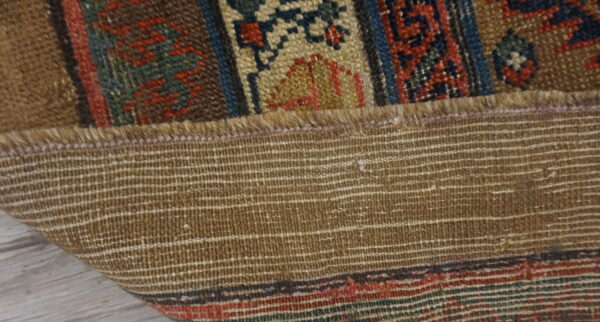 Close-up of a folded rug showing the woven brown backing and patterned red, blue, and tan pile.
