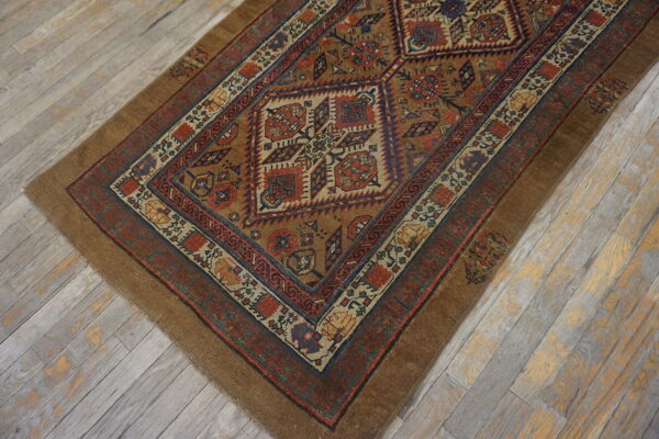 Tan and rust geometric rug with blue accents displayed on worn, wide plank grey flooring.