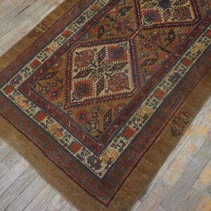 Geometric brown, red, and blue diamond patterned rug lying diagonally on whitewashed wood flooring.