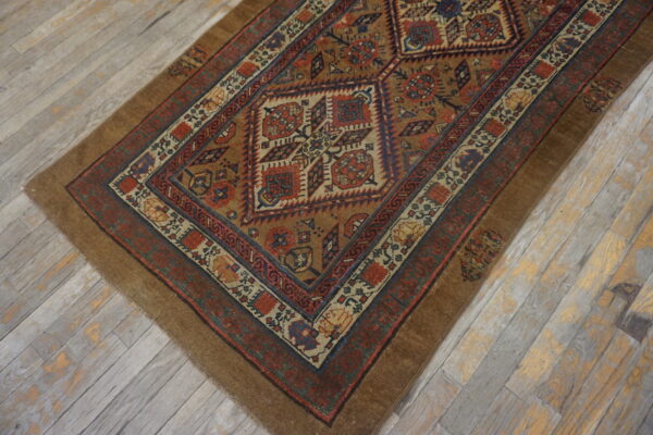 Geometric brown, red, and blue diamond patterned rug lying diagonally on whitewashed wood flooring.