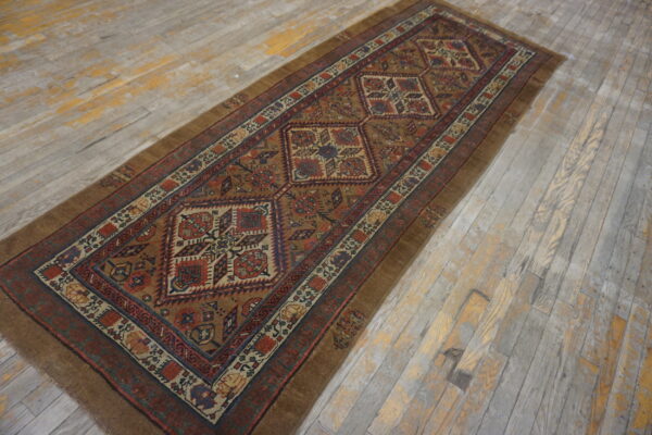 Brown and rust geometric runner rug displayed lengthwise on heavily distressed gray and yellow wood planks.