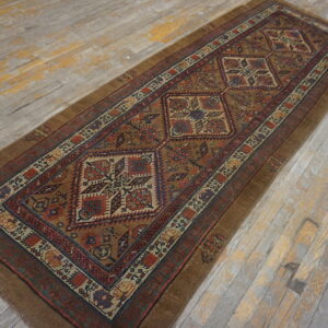 Geometric brown, red, and blue runner rug with central medallions rests on worn gray wood flooring.