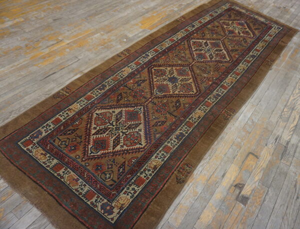 Geometric brown, red, and blue runner rug with central medallions rests on worn gray wood flooring.