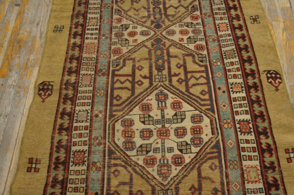 Low-pile runner with geometric medallions and multiple borders in gold, red, blue, and teal on wood planks.