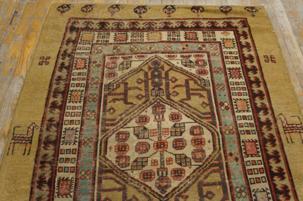 Mustard, teal, and rust low-pile rug with a complex geometric design resting on light wood flooring.