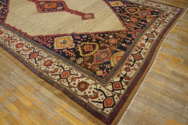 Intricate low-pile rug with a beige field and dark geometric border rests on aged hardwood planks.