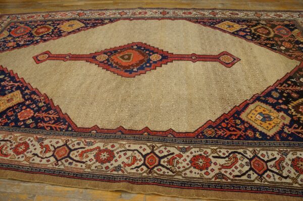 Geometric rug with a tan center field and dark blue, red, and brown tribal border designs on wood planks.