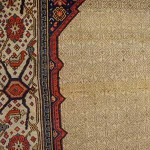 Detailed view of a rug corner with a beige textured field next to a red, blue, and cream patterned border.