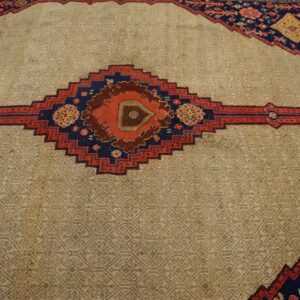 Low-pile beige rug field featuring a subtle geometric weave and a bold, centered red and navy traditional diamond.