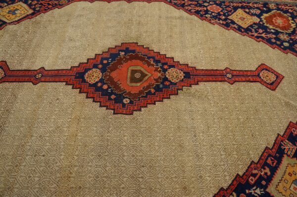 Low-pile beige rug field featuring a subtle geometric weave and a bold, centered red and navy traditional diamond.