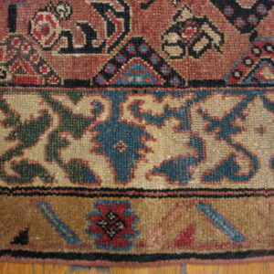 Low-pile rug detail showing russet, tan, and brown patterns across three borders on a wood floor.