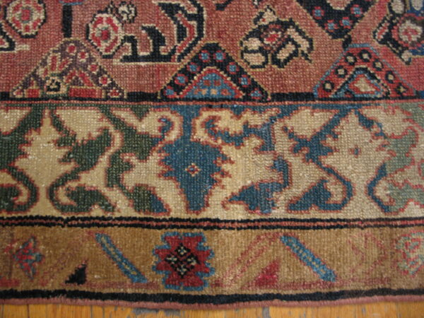 Low-pile rug detail showing russet, tan, and brown patterns across three borders on a wood floor.