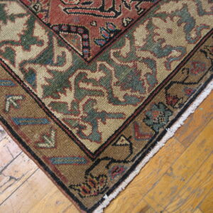 Rust and beige traditional rug corner with green accents and fringe rests on weathered wood planks.