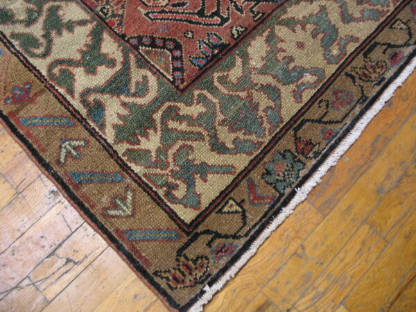 Rust and beige traditional rug corner with green accents and fringe rests on weathered wood planks.