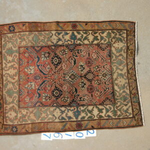Traditional patterned rug with red, blue, and green geometric details lying flat on light gray concrete.