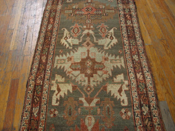 Muted geometric runner in sage green and rust orange covers a rustic wooden floor.